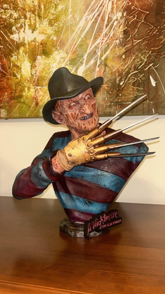 Figura de Freddy Krueger de 'Pesadilla en Elm Street', con guante de cuchillas y sombrero, sobre un pedestal en una mesa.